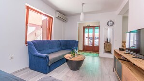 Ein modernes Wohnzimmer mit einem blauen Sofa, einem Couchtisch mit Flaschen, einem Fernseher und einem Holzschrank.