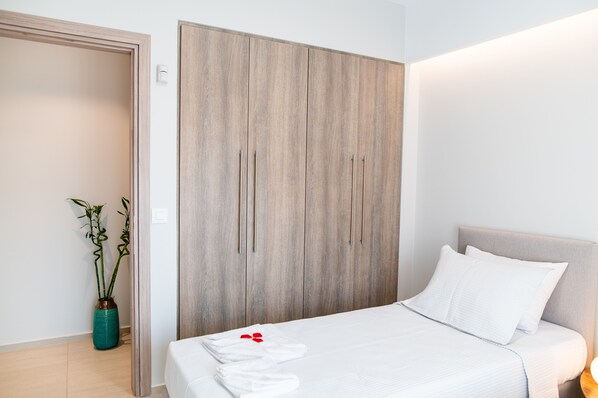A hotel room with a wooden wardrobe, a bed with white bedding, and a potted plant. - Lilium Apartment (Kos)