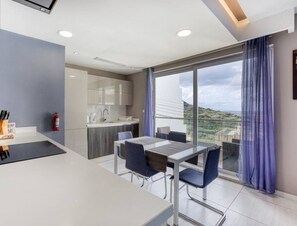 A modern hotel room with a dining area, kitchen, and large balcony with a view. - Stunning 2BR APT w/Hill View, perfect for Relaxing (Il-Mellieħa)