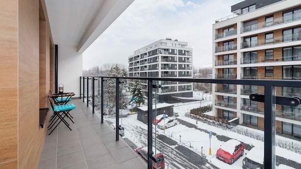 Un balcón con una mesa y sillas, con vista a una calle nevada y edificios.