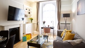 A modern living room with a flat-screen TV, a fireplace, a dining area with a table and chairs, and a sofa with cushions. - Avari Apartments - Winchester Collection (London)