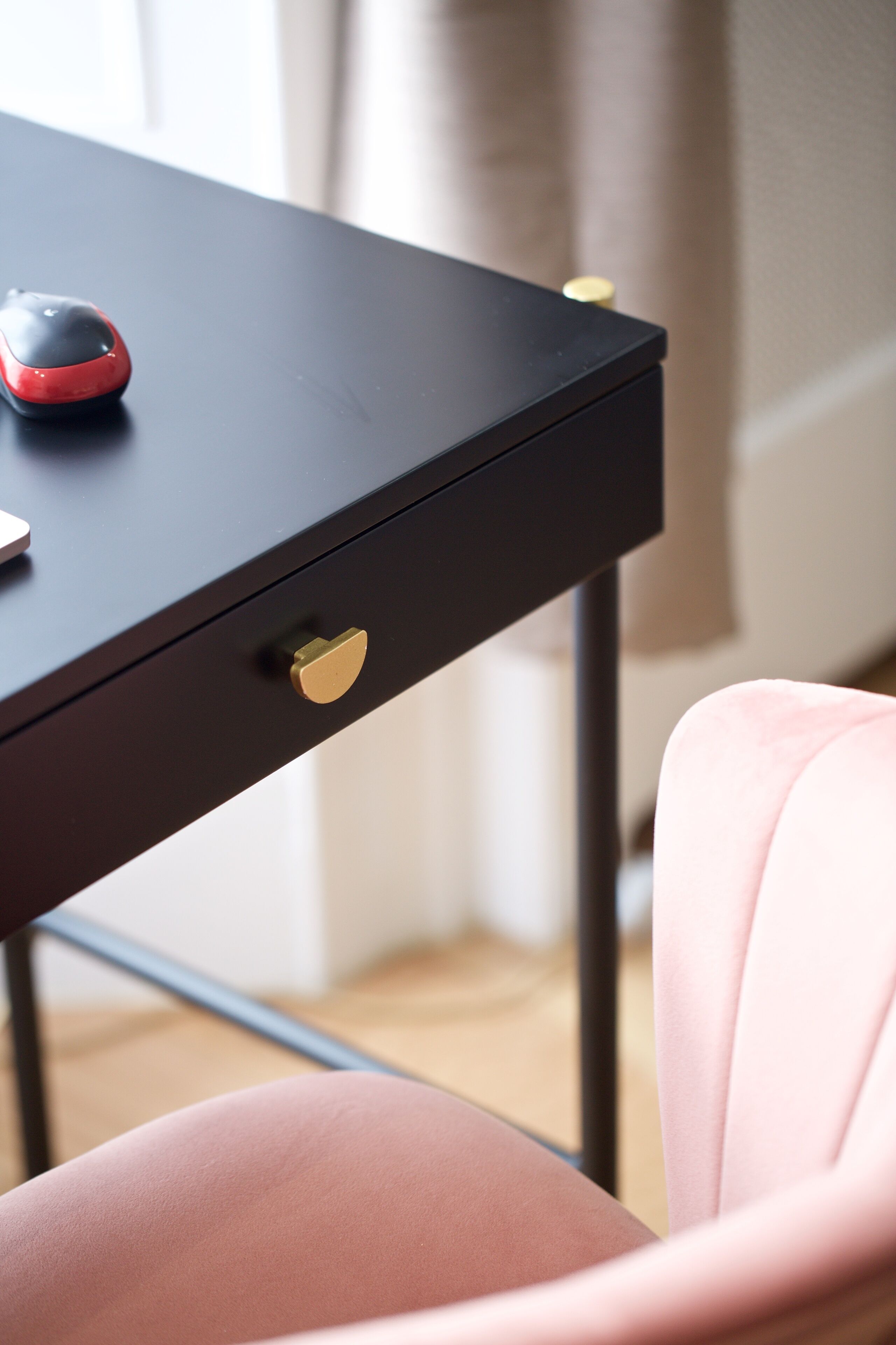A black desk with a red mouse and a gold drawer handle.