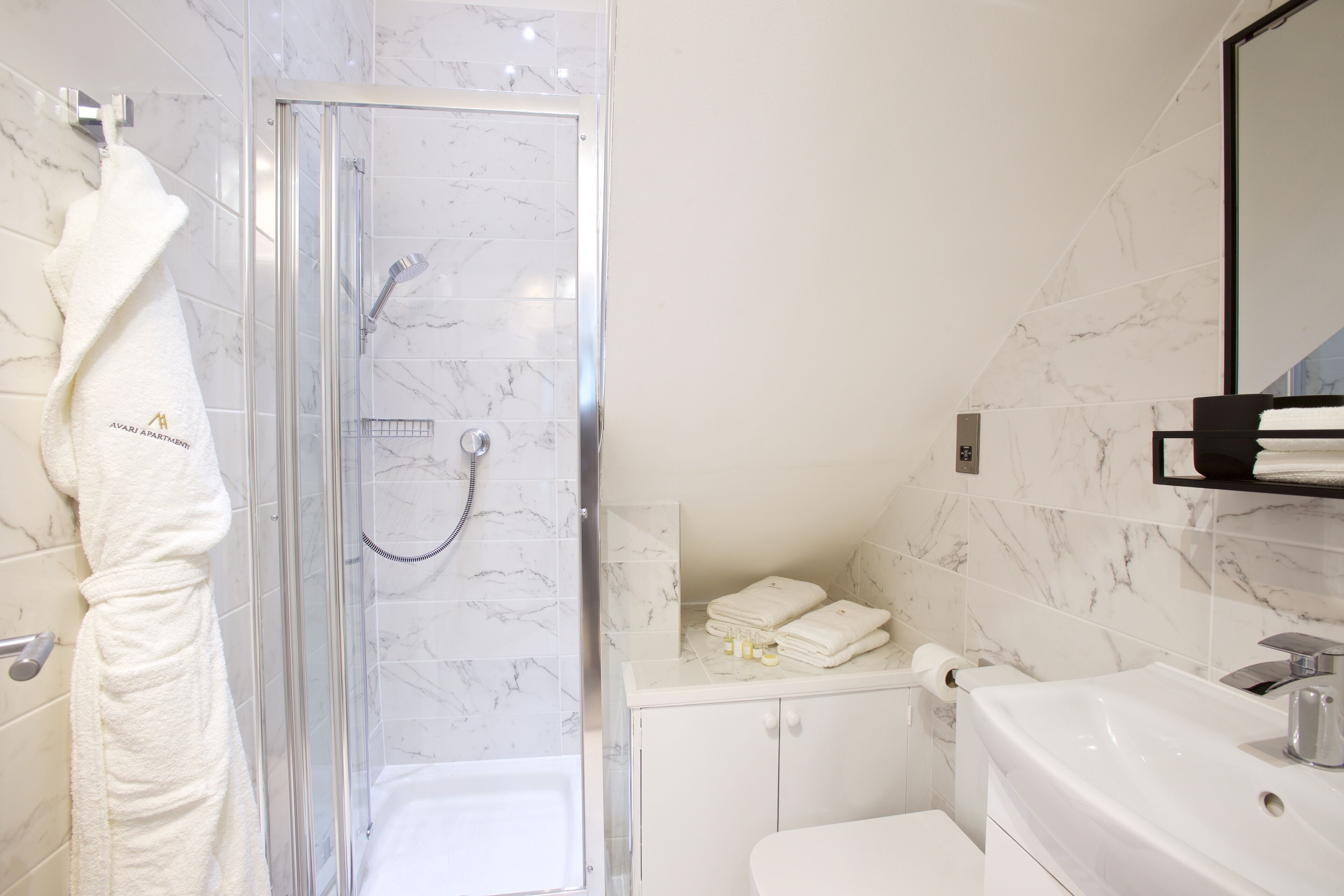 Une salle de bain moderne avec une douche à parois de verre, un lavabo blanc et un mur recouvert de carreaux de marbre.