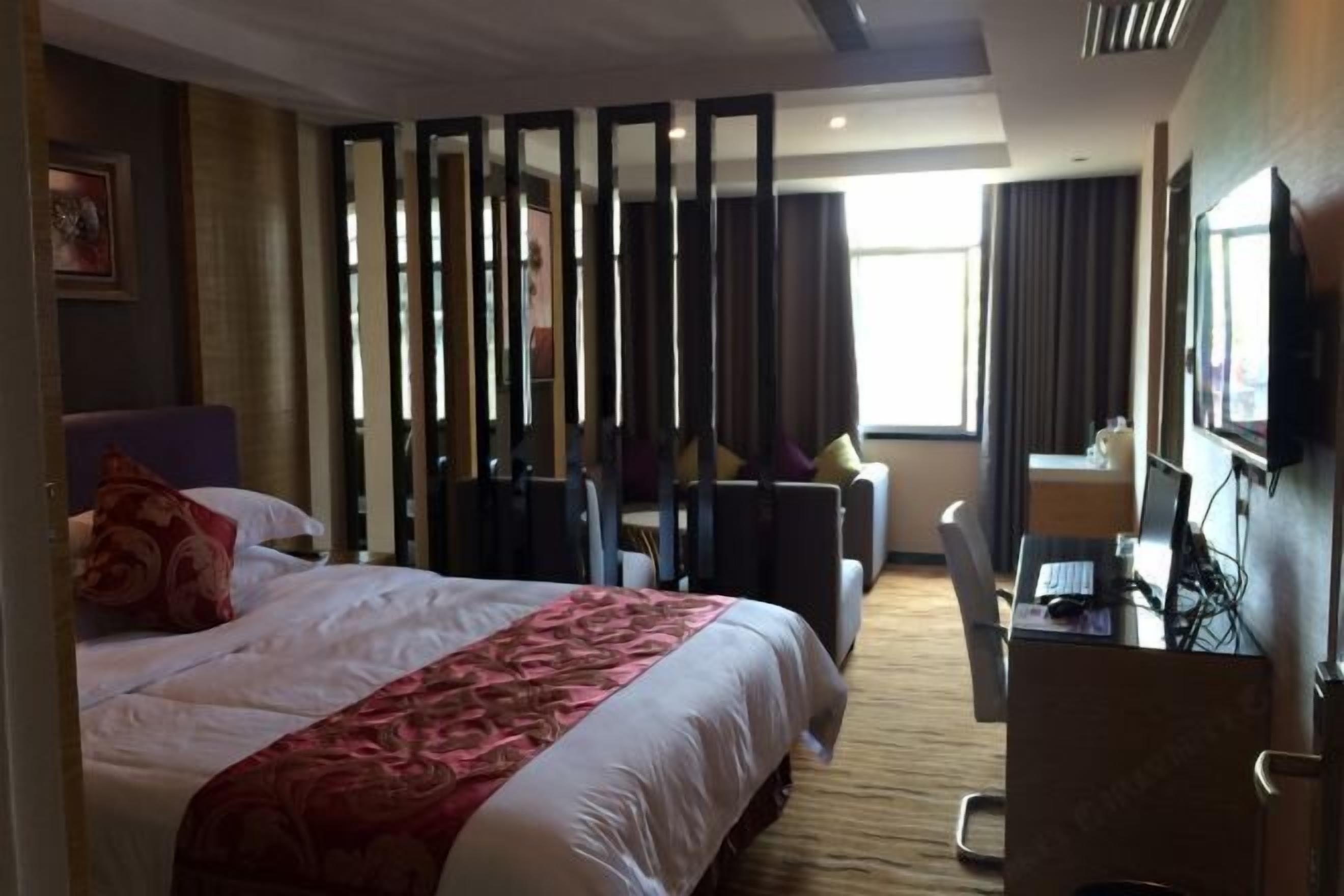 A hotel room with a bed, a desk with a computer, a chair, and a TV.