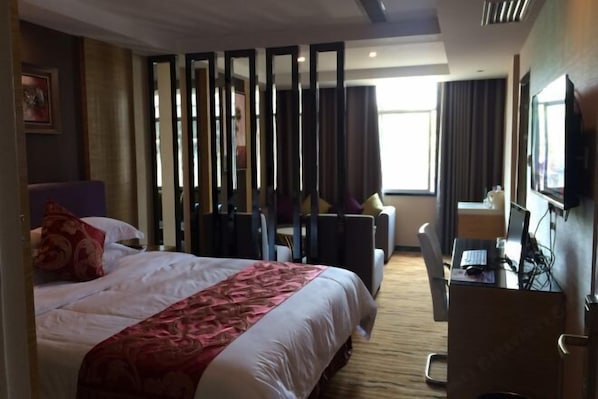 A hotel room with a bed, a desk with a computer, a chair, and a TV. - Mingjie Shanshui Hotel (Jianghua)