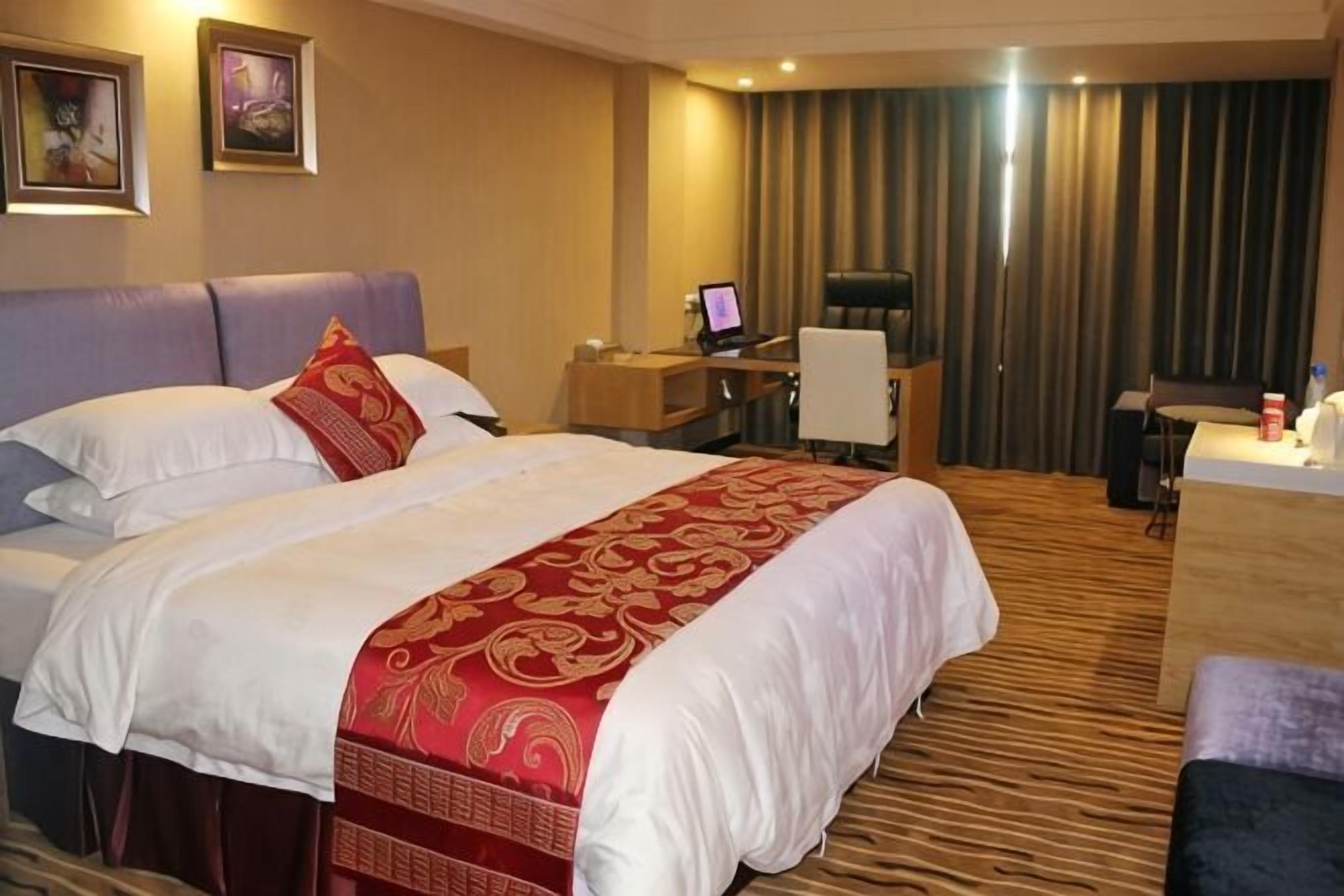 Een hotelkamer met een groot bed, een bureau met een computer, een stoel en een televisie.