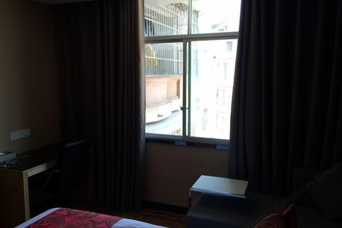 Habitación de hotel con cama, escritorio, una mesita y ventana con cortinas.