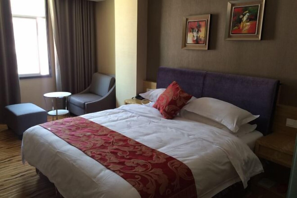 Habitación de hotel con cama, una silla, una mesita y dos cuadros en la pared.