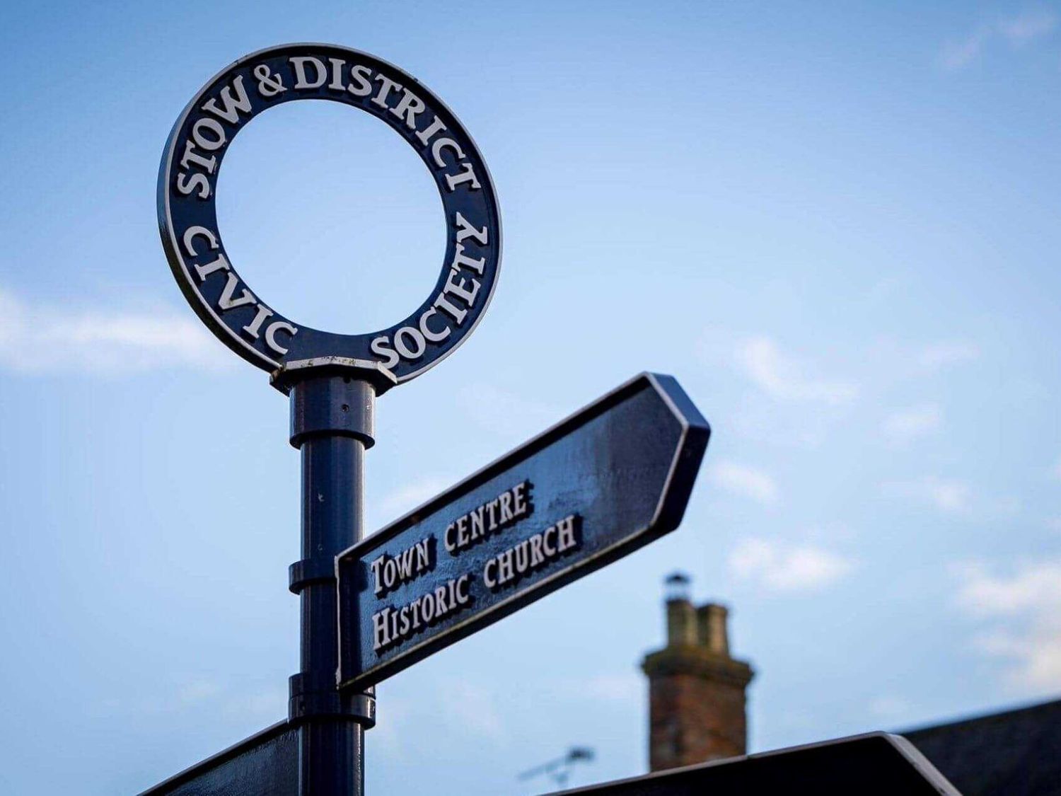 A signpost with a circular top reading "Stow & District Civic Society" and a directional sign pointing to "Town Centre Historic Church".