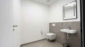 Un baño moderno con inodoro, lavamanos y cubo de basura.