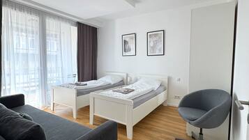 Una habitación de hotel moderna con dos camas individuales, un sofá gris, un escritorio y una silla.