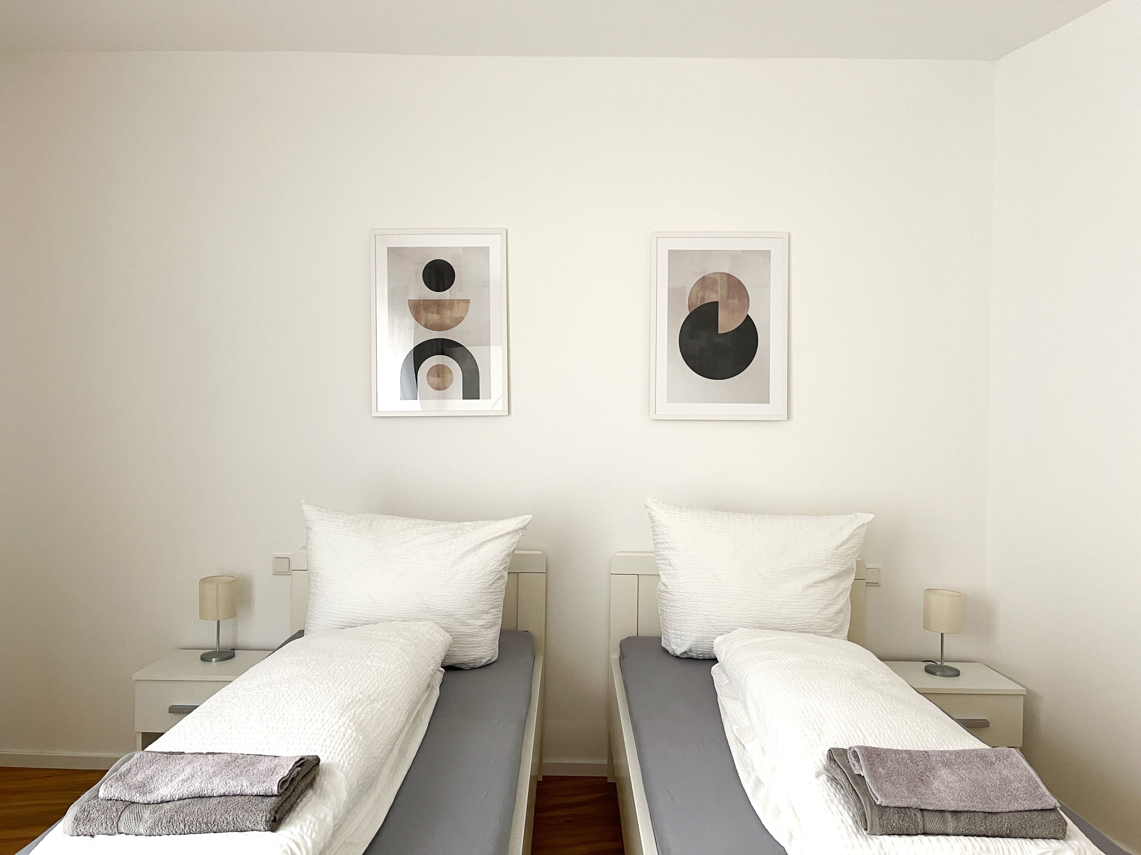 Una habitación con dos camas individuales, ropa de cama blanca y dos mesitas de noche con lámparas.