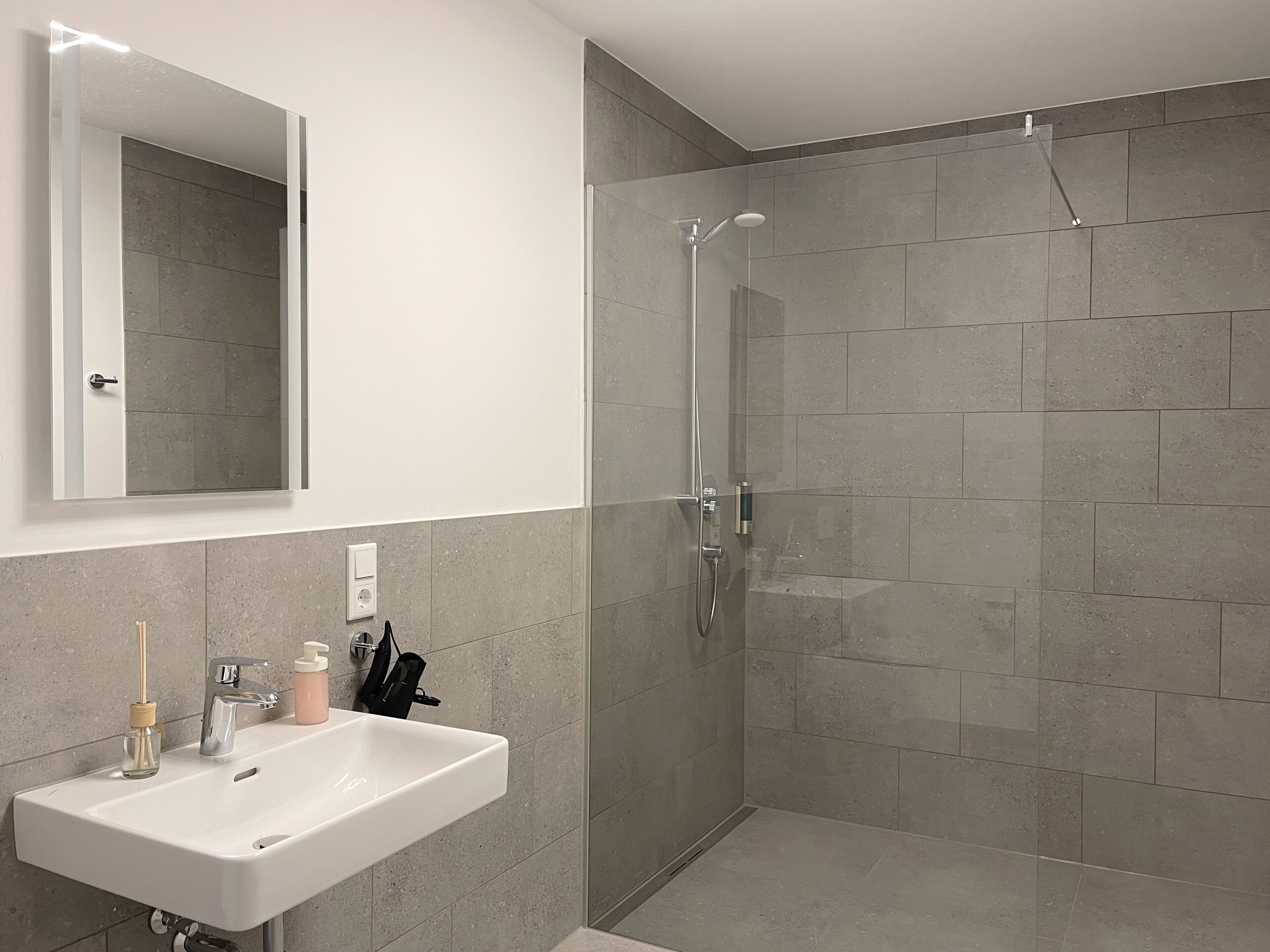 Ein modernes Badezimmer mit einer gläsernen Duschkabine, einem weißen Waschbecken und einem Spiegel darüber.