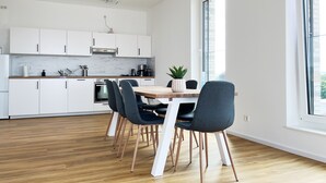Una cocina moderna con armarios blancos, un protector contra salpicaduras de mármol y una zona de comedor con una mesa y sillas de madera.