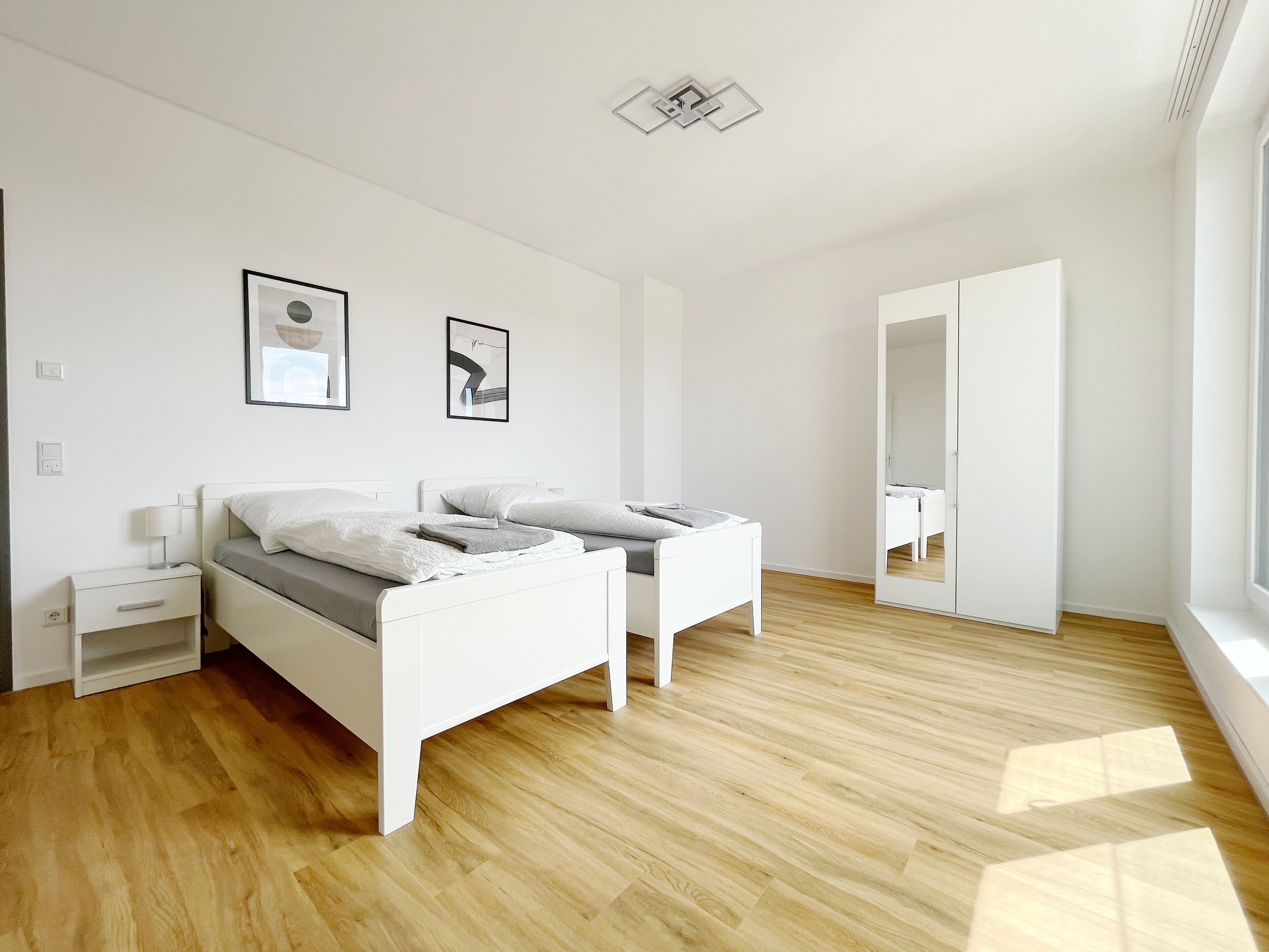 Une chambre moderne avec deux lits, une table de chevet, un miroir et une fenêtre.