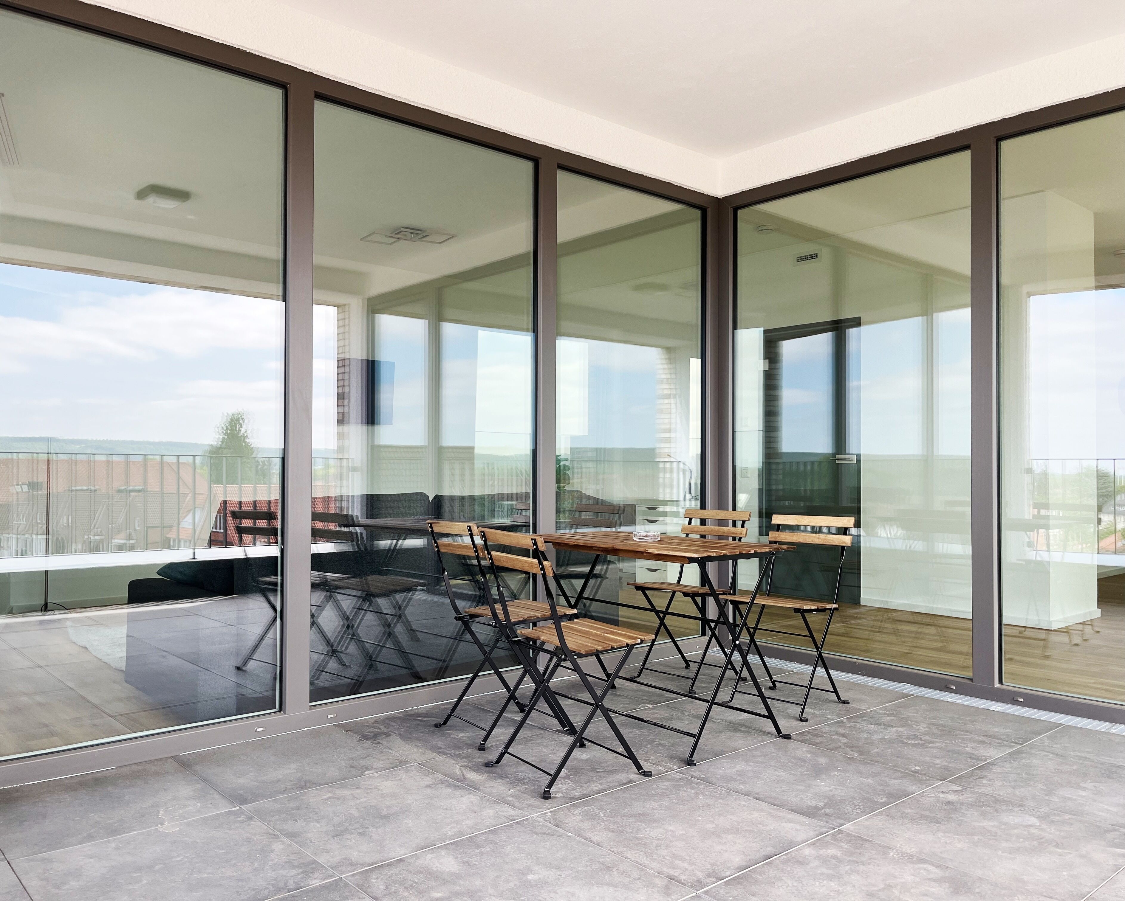 Ein moderner Balkon mit Glastrennwand, einem Holztisch und vier Stühlen.