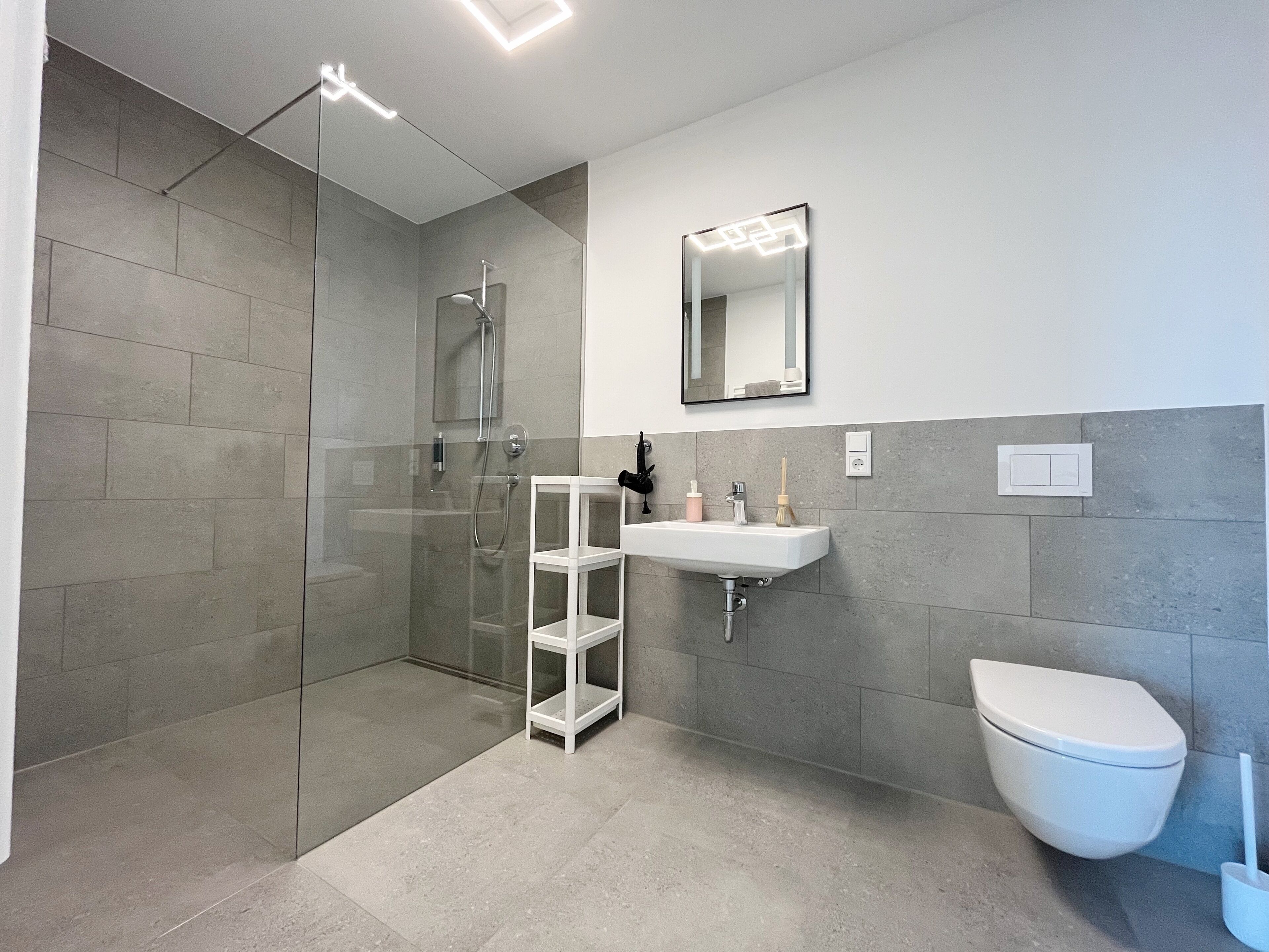 Un baño moderno con ducha de vidrio, un lavamanos blanco y un espejo encima, y un inodoro.