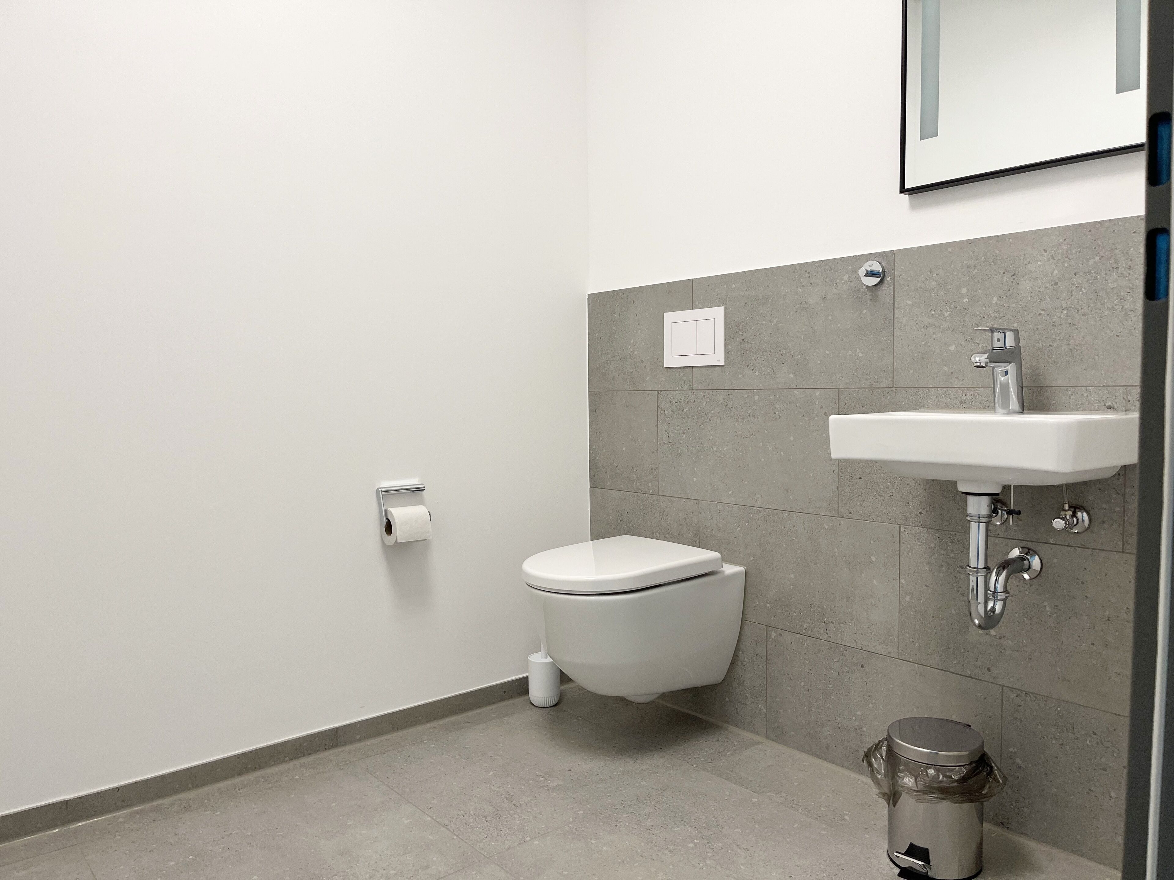 A modern bathroom with a toilet, sink, and trash bin.