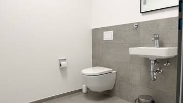 A modern bathroom with a toilet, sink, and trash bin.