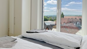 Un dormitorio con un ventanal grande, una cama con ropa de cama blanca y un armario blanco.