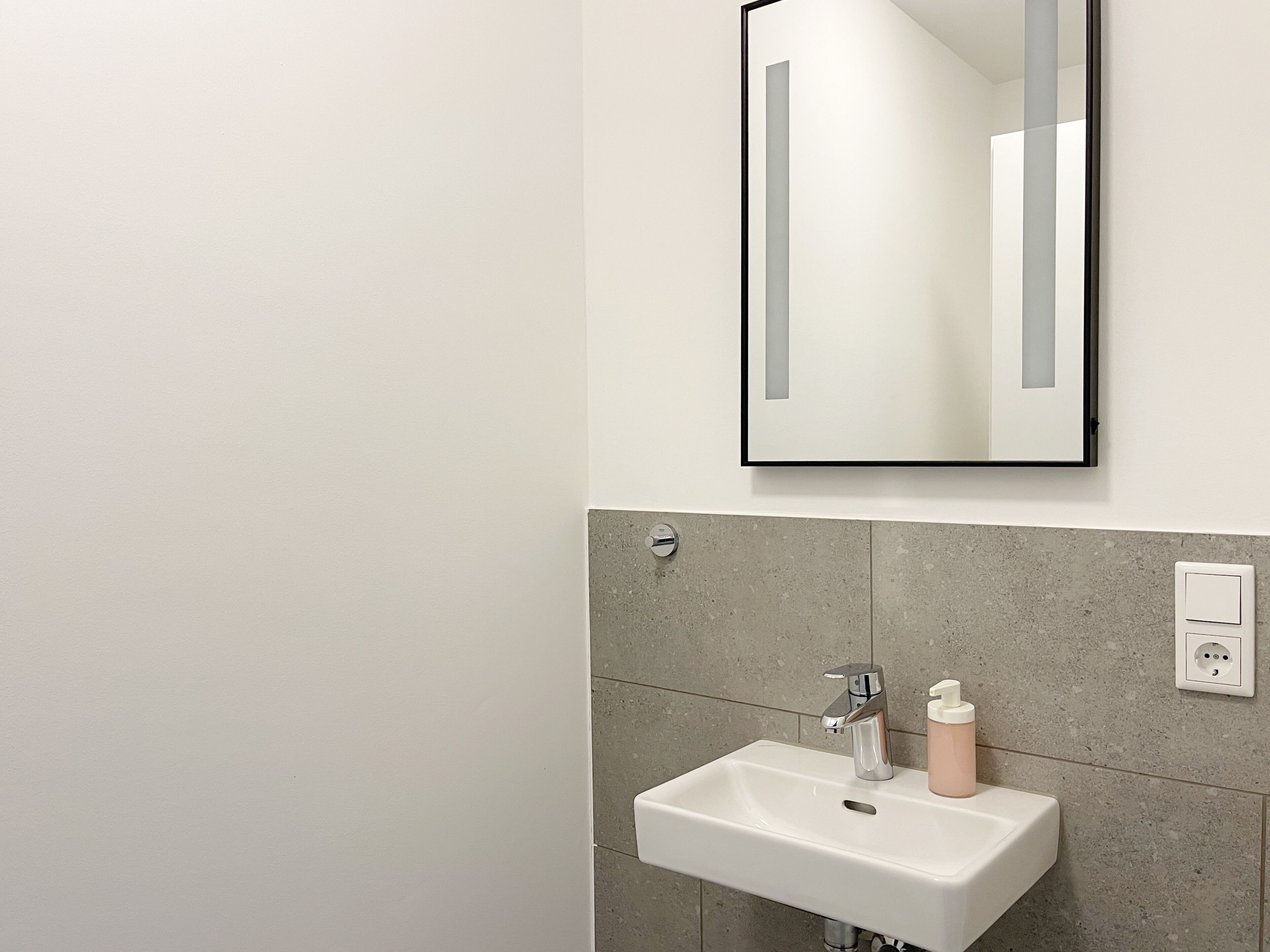 Une salle de bain moderne avec un lavabo blanc, un miroir et un distributeur de serviettes.