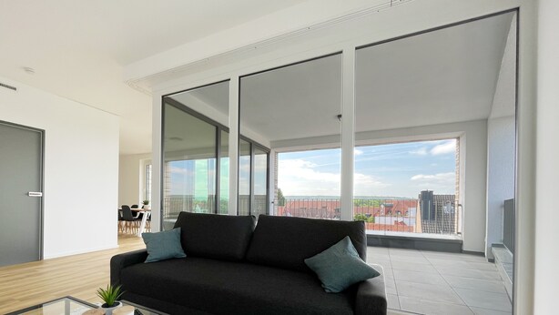 Una sala de estar moderna con un sofá negro, una mesa de centro de vidrio y vistas de la ciudad a través de amplios ventanales.