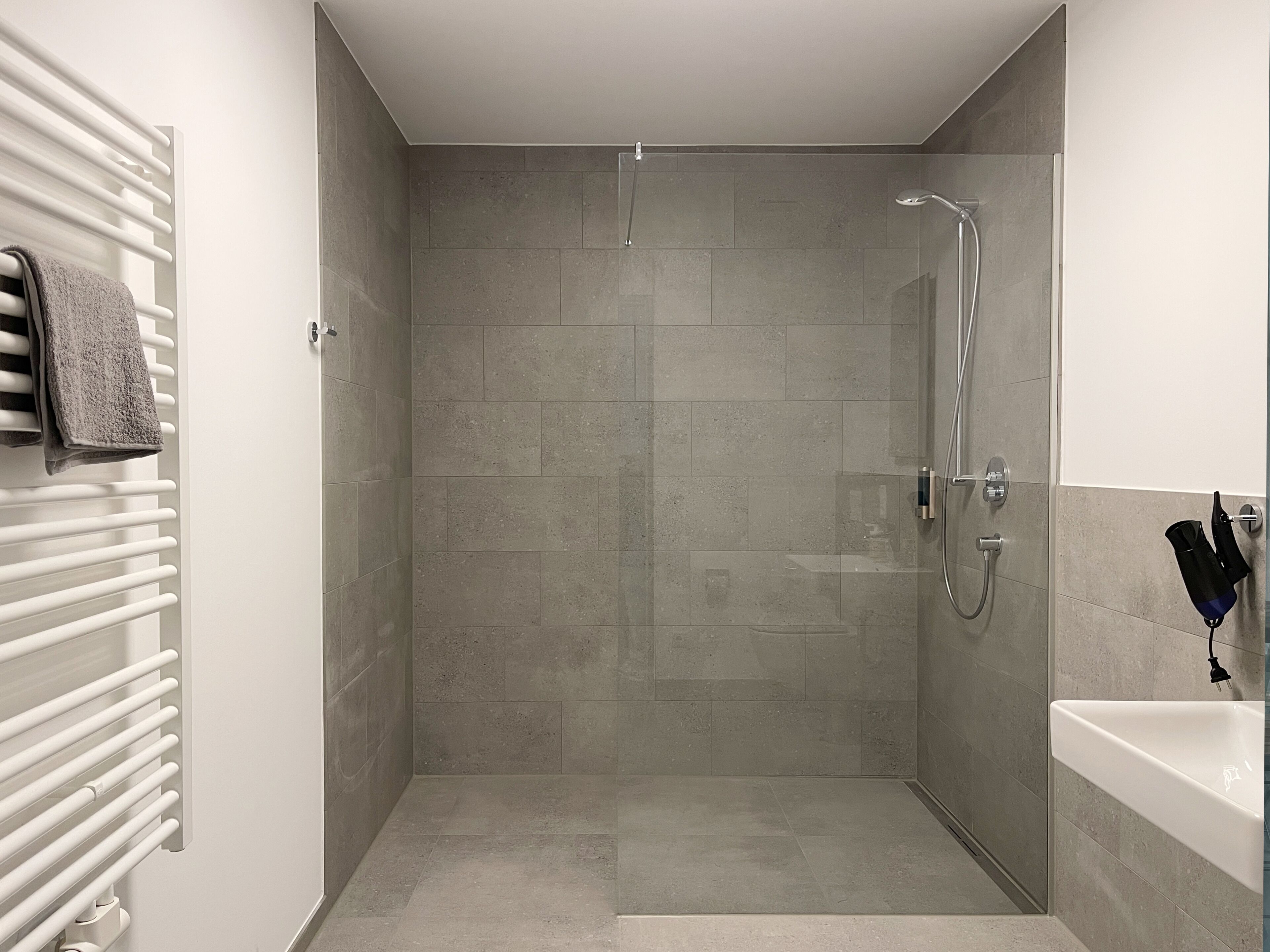 A modern bathroom with a glass-enclosed shower, a white sink, and a towel rack.