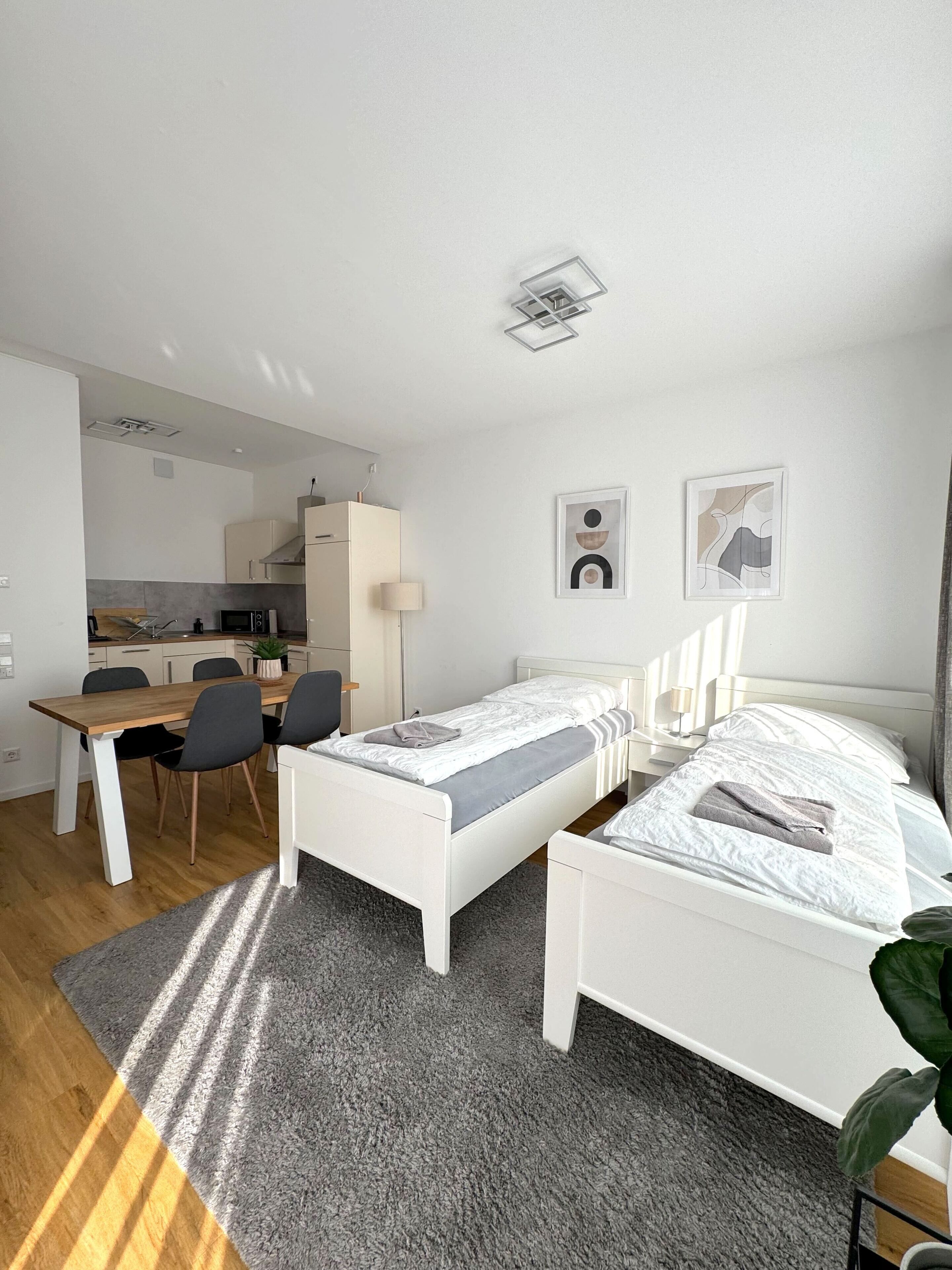 A modern, minimalist room with two single beds, a small kitchen area, and a dining table.