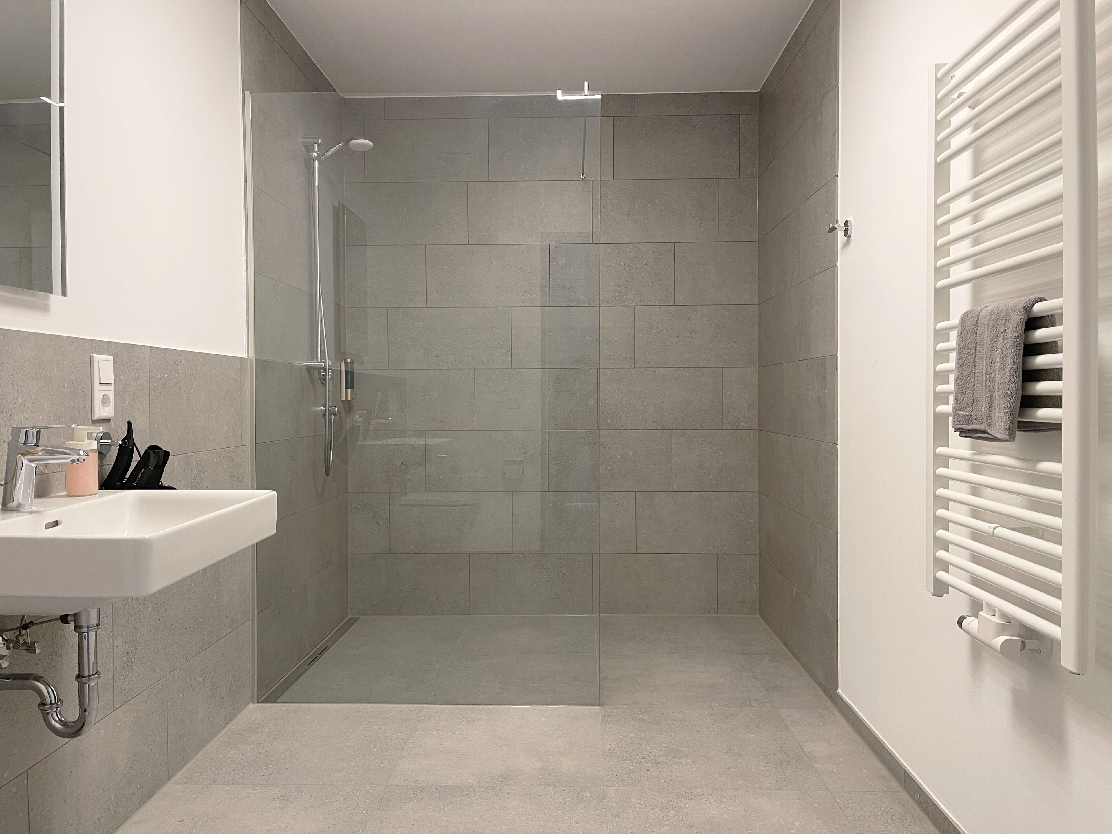 A modern bathroom with a glass-enclosed shower, a white sink, and a towel rack.