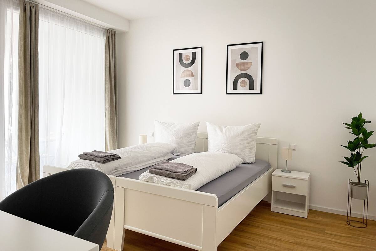 A modern bedroom with a bed, bedside tables, a chair, and a potted plant.
