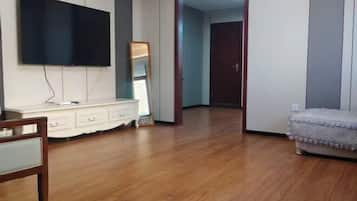 Ein Zimmer mit einem an der Wand befestigten Flachbildfernseher, einer weißen Kommode, einem Spiegel und einem Bett mit gemustertem Bettbezug.