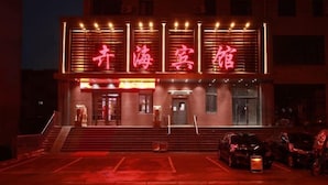 A hotel with a prominent red neon sign, a staircase leading to the entrance, and a parking area with several cars. - Huihai Hotel (Xinbin)