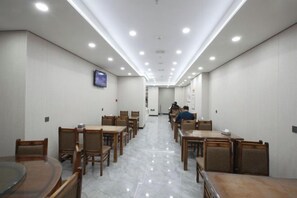 A hotel dining area with multiple wooden tables and chairs, recessed ceiling lighting, and a television on the wall. - Huihai Hotel (Xinbin)