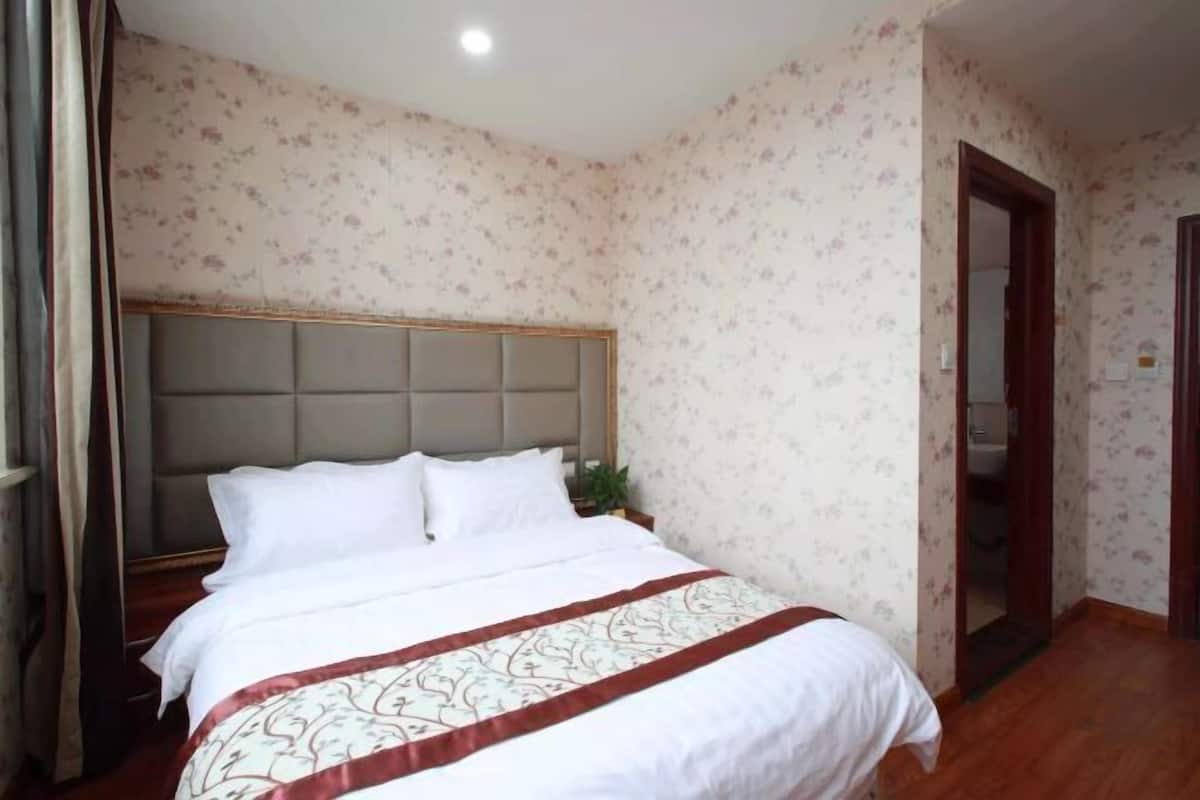 A bedroom with a bed, floral wallpaper, and a wooden door.
