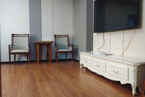 A room with two wooden chairs, a small table, a white dresser, and a mounted flat-screen TV. - Huihai Hotel (Xinbin)