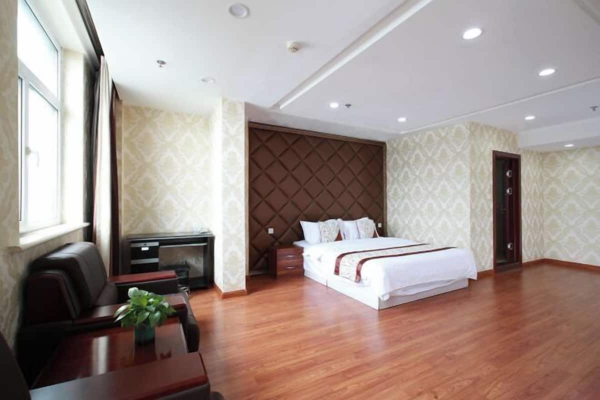 A hotel room with a large bed, a desk, a chair, a small table with a plant, and a wardrobe.