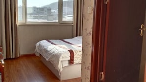 A bedroom with a bed, wooden floor, window, and a door. - Huihai Hotel (Xinbin)