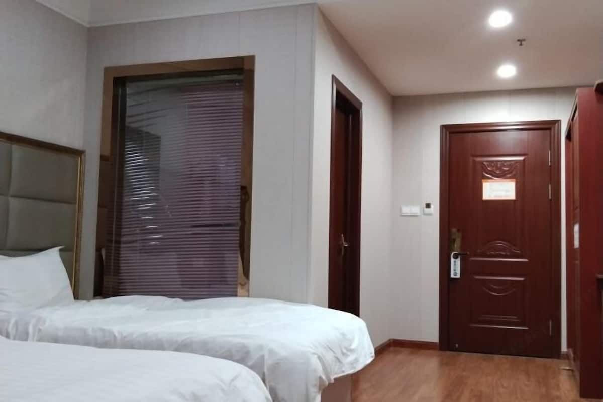 A hotel room with two beds, a wooden door, and a window with blinds.