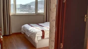 A bedroom with a bed, wooden flooring, a window, and a door.
