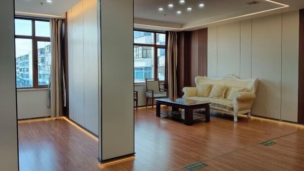 A modern hotel room with a wooden floor, a sofa, a coffee table, and large windows offering a view of the city. - Huihai Hotel (Xinbin)