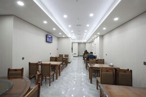 Un comedor de hotel con varias mesas y sillas, un televisor en la pared y un ambiente limpio y bien iluminado.