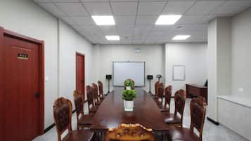 Un salón de conferencias con una larga mesa, sillas, una pizarra y una planta.