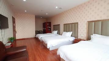 Habitación de hotel con tres camas, un televisor, piso de madera y un armario rojo.