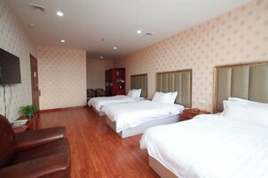 Habitación de hotel con tres camas, un televisor, piso de madera y un armario rojo.