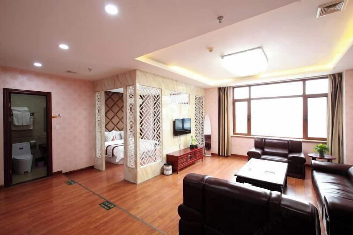 A hotel room with a living area, a sofa set, a television, and a large window.