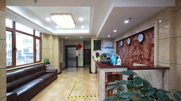 A hotel lobby with a reception desk, a sofa, a large window, and a plant.