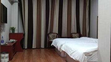 Habitación de hotel con suelo de madera, cama con ropa blanca, escritorio con teléfono y una planta, y una silla.