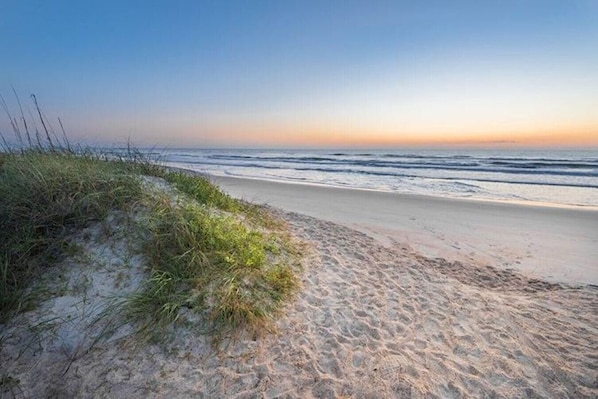 A beach with sand and grass, leading to the ocean.