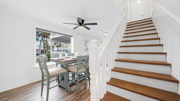 A spacious room with a wooden staircase, a ceiling fan, and a dining area with chairs and a table.