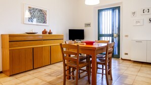 Ein Essbereich mit Holztisch und Stühlen, einem Fernseher und einer Küchenzeile mit Schränken.